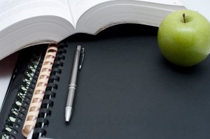 Education and learning background with a fresh healthy green apple alongside an open book with a pen and spiral binders
